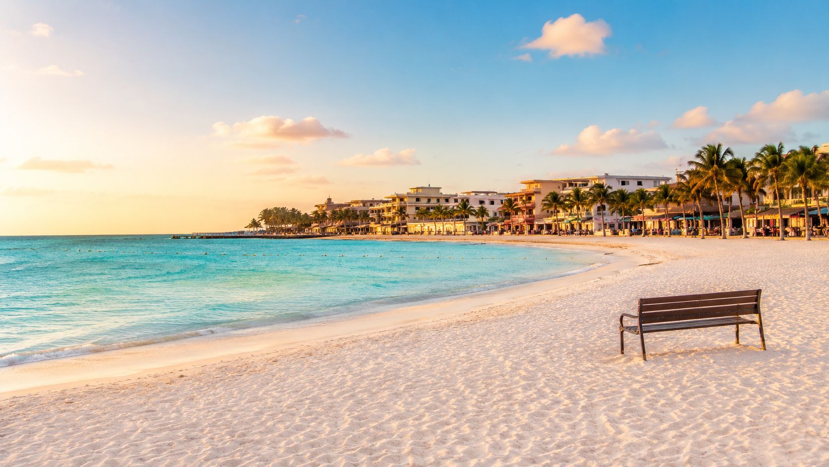 Un banco de madera vacío frente a una playa paradisíaca con aguas turquesas al atardecer en México.