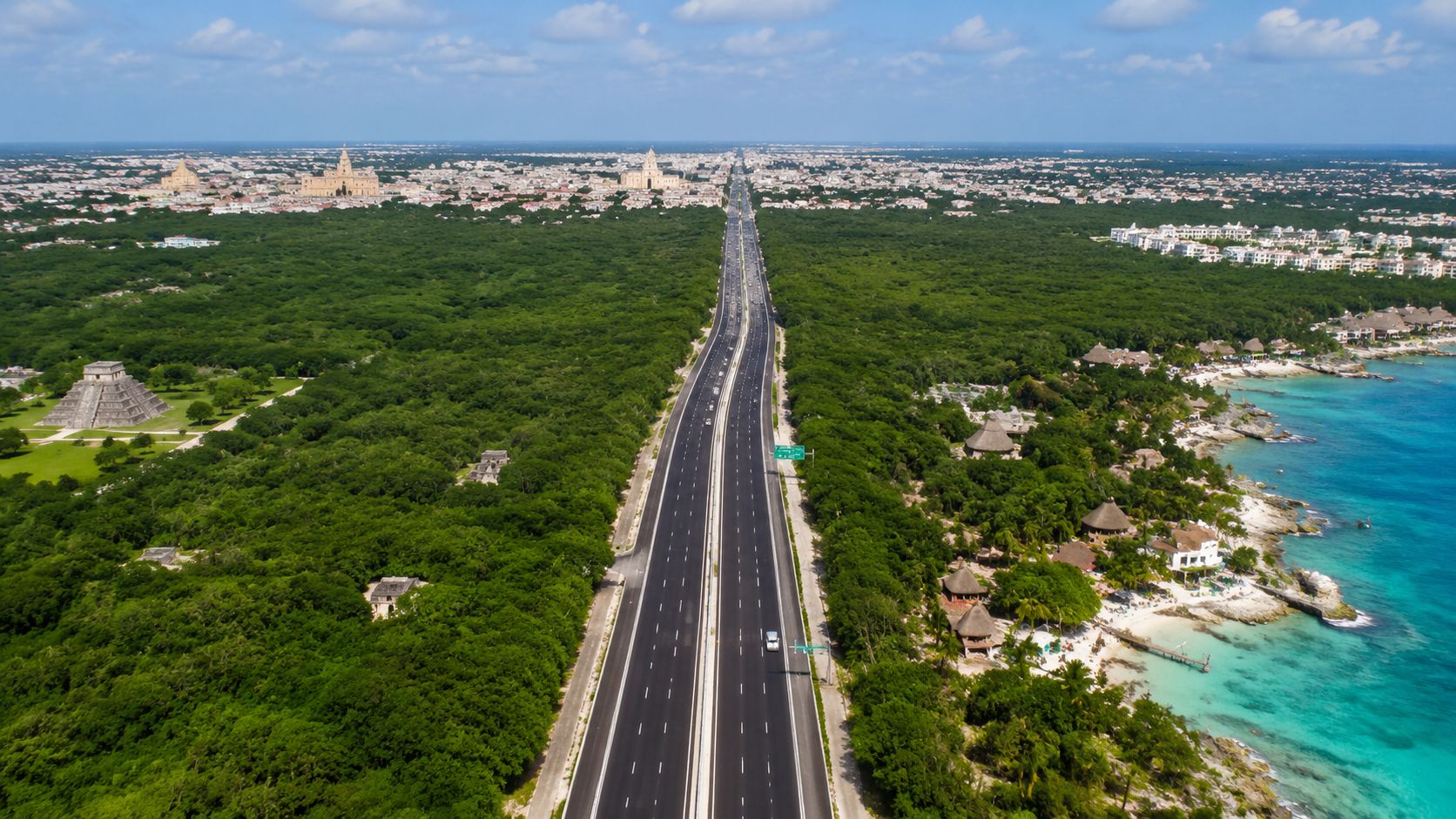 Una carretera moderna atraviesa una densa selva verde junto a ruinas mayas y el mar caribeño.